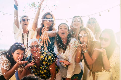 Group of people celebrate together having a lot of fun blowing coloured confetti - friendship and diversity ages generation laugh and smile on party - cheerful joyful concept for ladies