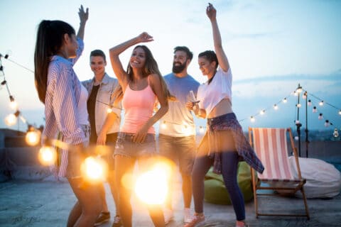 Leisure, celebration and people concept - happy friends with drinks toasting at rooftop party at night
