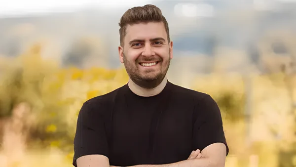 Massimo Squillance, freundlicher Ansprechpartner bei eventflotte.de, lächelnd mit verschränkten Armen vor unscharfem, gelbem Hintergrund.